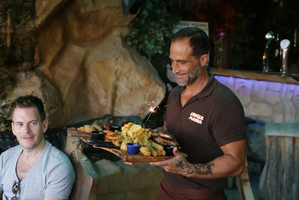 A member of staff carrying a wooden sharing platter of ribs and fries, lit by a sparkler