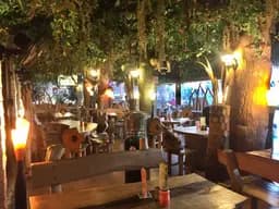 Jungle Mania's dining room at night, lit by torches beneath a canopy of leaves