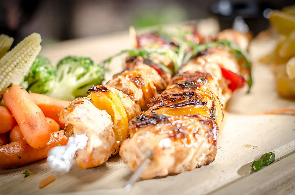 Grilled chicken skewers with baby corn, broccoli and carrots on a wooden board
